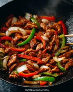 Black pepper chicken stir-fry with colorful bell peppers and onions in a cast iron skillet