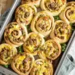 Golden breakfast rolls filled with eggs, sausage, bacon, and cheese in a baking tray, garnished with parsley