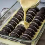 Oreo Dump Cake (Easy 5-Ingredient Dessert) 6 Pouring creamy batter over stacked chocolate sandwich cookies in a baking dish for Oreo dump cake