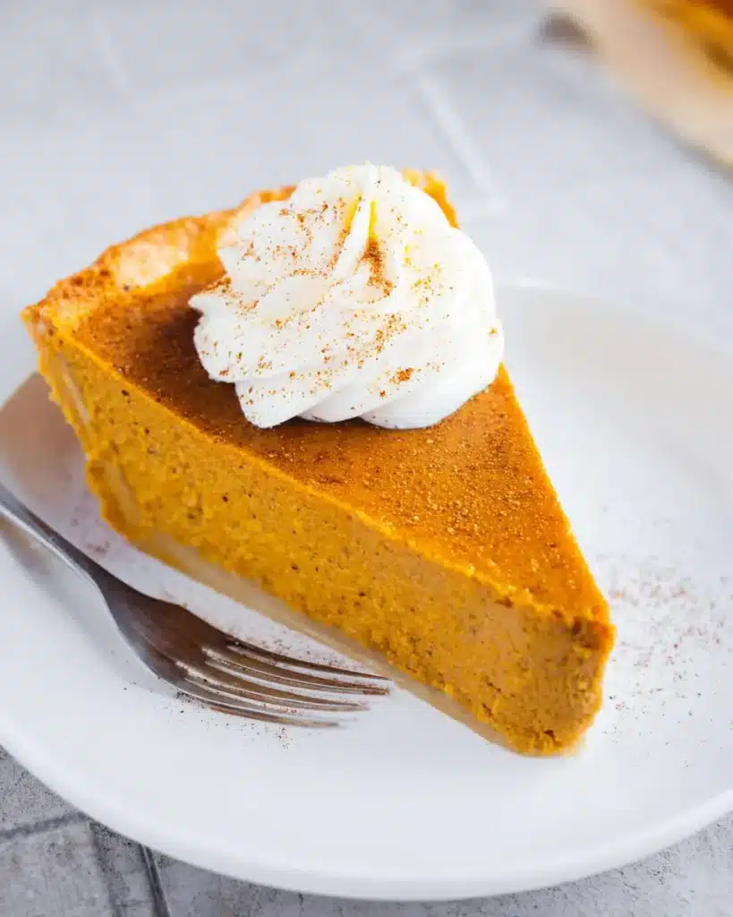 Pumpkin Pie with Sweetened Condensed Milk | Remarkable Creamy Favorite 11 Close-up of a slice of pumpkin pie with whipped cream and flaky crust on a white plate