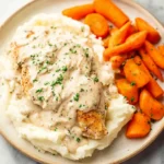 Cream Cheese Chicken (Easy & Creamy One-Skillet Dinner) 12 Cream cheese chicken with mashed potatoes and carrots on a beige plate, topped with creamy herb sauce and fresh parsley.
