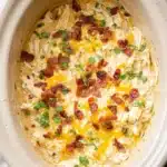 Cheesy Crockpot Crack Chicken topped with crispy bacon and herbs in a slow cooker