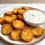 Crispy air fryer fried pickles served on a white plate with creamy dill dipping sauce in a glass bowl.