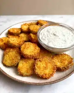 Crispy air fryer fried pickles served on a white plate with creamy dill dipping sauce in a glass bowl.