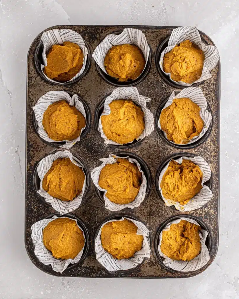 Easy Pumpkin Muffins (One-Bowl Fall Favorite!) 9 Unbaked easy pumpkin muffins in parchment liners spaced in a vintage muffin tin, ready to go into the oven.