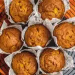 Easy Pumpkin Muffins (One-Bowl Fall Favorite!) 12 Freshly baked easy pumpkin muffins in parchment wrappers on a cooling rack, golden brown with cracked tops.