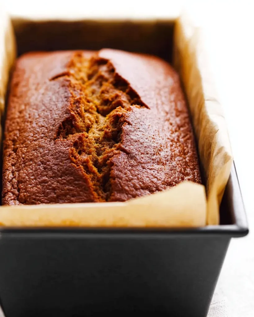 Pumpkin Muffins – Soft, Spiced, and Perfect Every Time 10 Freshly baked pumpkin bread cooling in a black loaf pan with parchment lining
