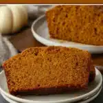 Moist pumpkin bread slices on a plate with a rich crumb texture and warm autumn background