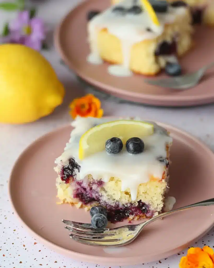 Close-up of lemon blueberry sheet cake with lemon glaze and fresh blueberry garnish on a plate