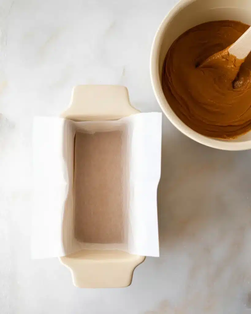 Parchment-lined loaf pan next to pumpkin bread batter in mixing bowl

