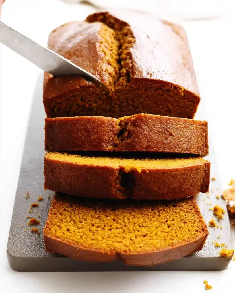 Freshly sliced pumpkin bread with golden crust and moist spiced interior on a cutting board