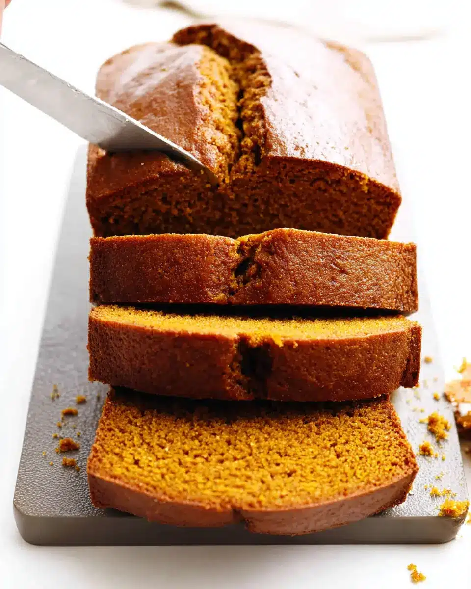 Freshly sliced pumpkin bread with golden crust and moist spiced interior on a cutting board