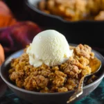 Warm pumpkin crisp dessert topped with vanilla ice cream in a dark bowl, showing crumbly streusel and creamy textures.