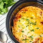 Slow Cooker Chicken Enchilada Casserole: Easy, Cheesy Comfort 9 Slow cooker chicken enchilada casserole topped with melted cheese and herbs in a black Crockpot with spoon and cilantro on the side