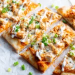 Sliced buffalo chicken flatbread with melted cheese, buffalo sauce, and green onions on parchment paper.