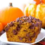 Moist chocolate chip pumpkin bread slice on white plate with autumn decorations in the background