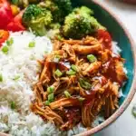 Bowl of shredded teriyaki chicken with rice, broccoli, and red bell peppers, garnished with green onions.