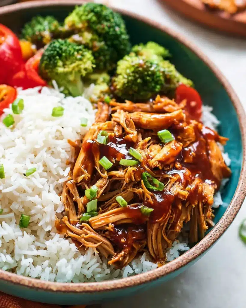 Bowl of shredded teriyaki chicken with rice, broccoli, and red bell peppers, garnished with green onions.