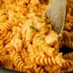 Close-up of buffalo chicken pasta with ranch sauce and rotini, garnished with herbs and served on a wooden spoon.