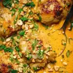 One Pan Coconut Lime Chicken Recipe with Creamy Sauce 9 Close-up of creamy coconut lime chicken thighs topped with chopped peanuts, scallions, and cilantro in a rich orange sauce