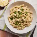 Crockpot Garlic Parmesan Chicken Pasta That's Creamy and Comforting 17 Bowl of creamy garlic parmesan rotini pasta with fresh parsley and a side of grated parmesan cheese on a rustic table.