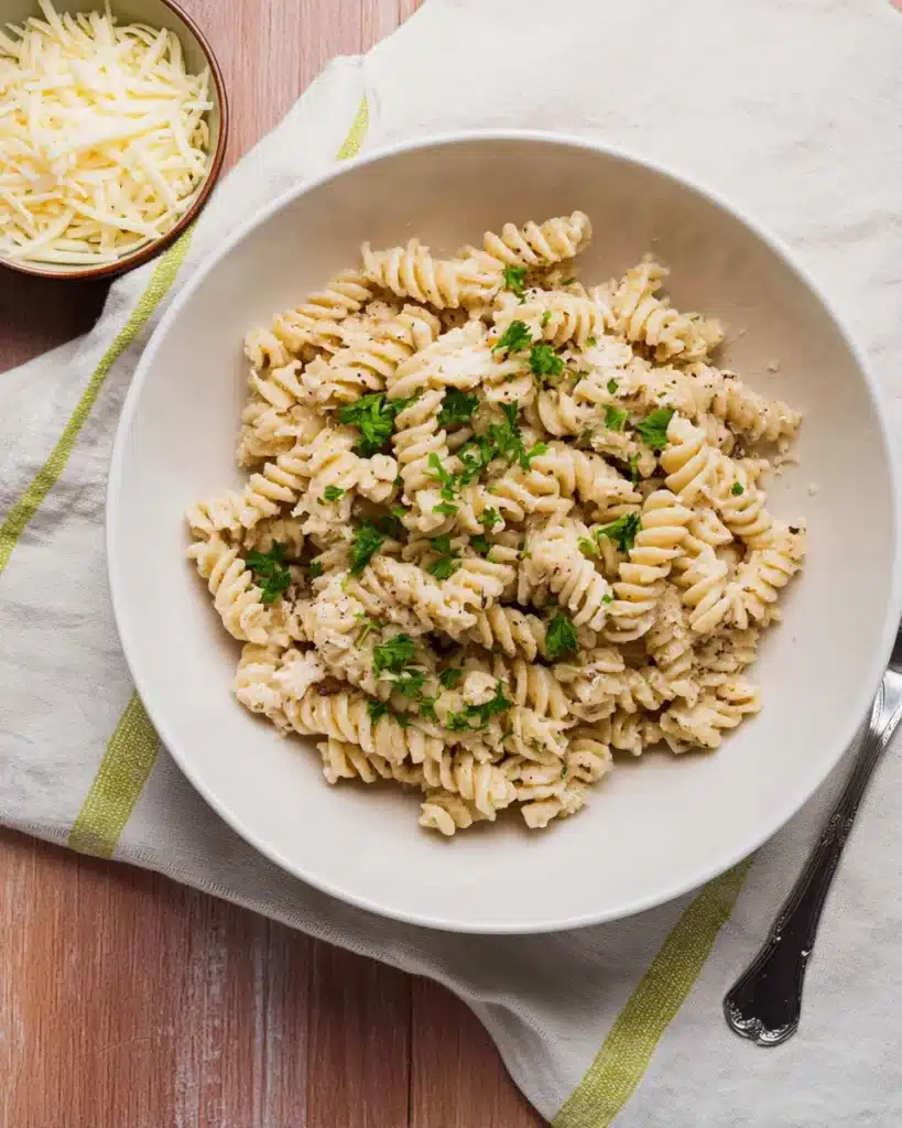 Crockpot Garlic Parmesan Chicken Pasta That's Creamy and Comforting 12 Bowl of creamy garlic parmesan rotini pasta with fresh parsley and a side of grated parmesan cheese on a rustic table.