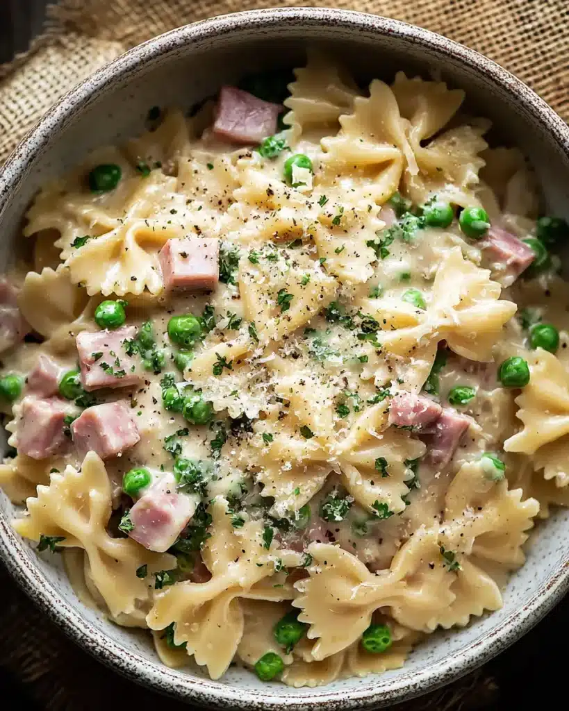 Rustic bowl of creamy farfalle pasta with ham, peas, Parmesan, and parsley on a burlap cloth.