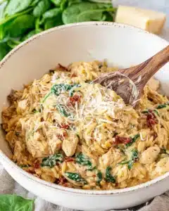 Creamy Tuscan chicken orzo in a white bowl with spinach, sun-dried tomatoes, and grated Parmesan