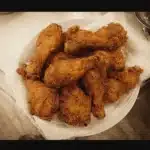 Golden-brown crispy fried chicken drumsticks on a plate lined with paper towels.