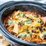 Crockpot Chicken Enchilada Casserole – Cheesy Comfort in Every Bite 11 Slow cooker chicken enchilada casserole with melted cheese, black beans, tortilla strips, and cilantro in a crockpot.