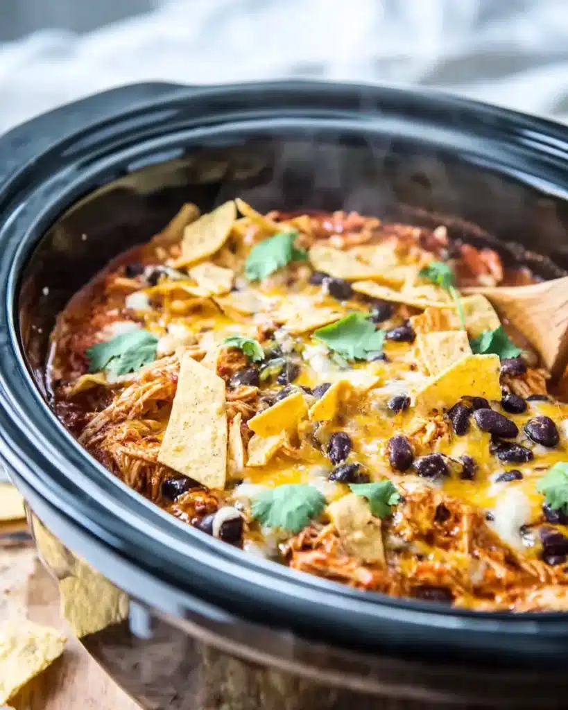 Crockpot Chicken Enchilada Casserole – Cheesy Comfort in Every Bite 8 Slow cooker chicken enchilada casserole with melted cheese, black beans, tortilla strips, and cilantro in a crockpot.