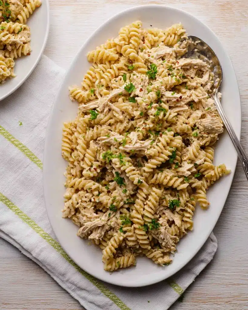 Crockpot Garlic Parmesan Chicken Pasta That's Creamy and Comforting 16 Creamy garlic parmesan rotini pasta with shredded chicken and parsley on a white platter.