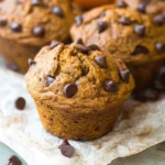 Moist pumpkin chocolate chip muffin topped with mini chocolate chips on parchment paper