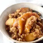 Warm apple crisp dessert with cinnamon-baked apples and golden oat topping in a white bowl