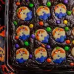 Glass baking dish filled with Halloween brookies topped with ghost cookies and colorful M&M candies on a festive background.