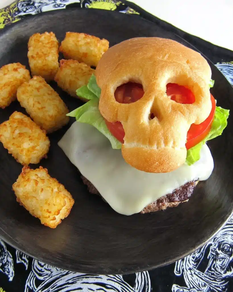 Halloween cheeseburger skull with golden bun, melted cheese patty, lettuce, tomato, and crispy tater tots on a plate