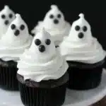 Chocolate cupcakes topped with ghost-shaped white frosting decorated with black eyes and mouth, perfect for Halloween treats.