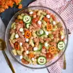 Halloween Pasta Salad – A Fun and Spooky Side Dish 14 “Halloween pasta salad with carved cucumber jack-o-lanterns, tricolor rotini, mozzarella pearls, cherry tomatoes, and carrots in a glass bowl on a rustic table.”