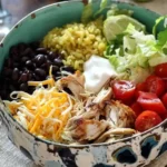 70+ Easy Rotisserie Chicken Recipes for Fast, Flavorful Weeknight Meals 9 Colorful rotisserie chicken burrito bowl with avocado, black beans, cheese, rice, and fresh toppings in a patterned bowl