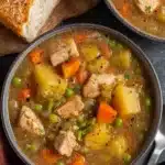 Slow Cooker Chicken Stew Recipe for a Hearty, Happy Dinner 11 Hearty slow cooker chicken stew in bowls with potatoes, carrots, celery, peas, and tender chicken, served with crusty artisan bread on a rustic table.