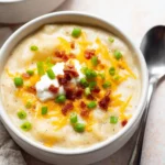 Loaded Baked Potato Soup Recipe for Cozy Nights 11 Creamy loaded baked potato soup topped with melted cheddar, crispy halal meat, sour cream, and fresh scallions in a white bowl.