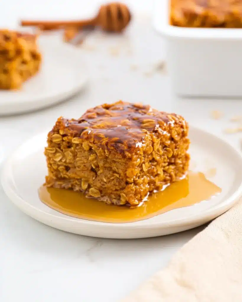Close-up of a slice of pumpkin baked oatmeal drizzled with honey on a white plate