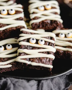 Halloween mummy brownies with white chocolate drizzle and candy eyeball decorations on a rustic table.