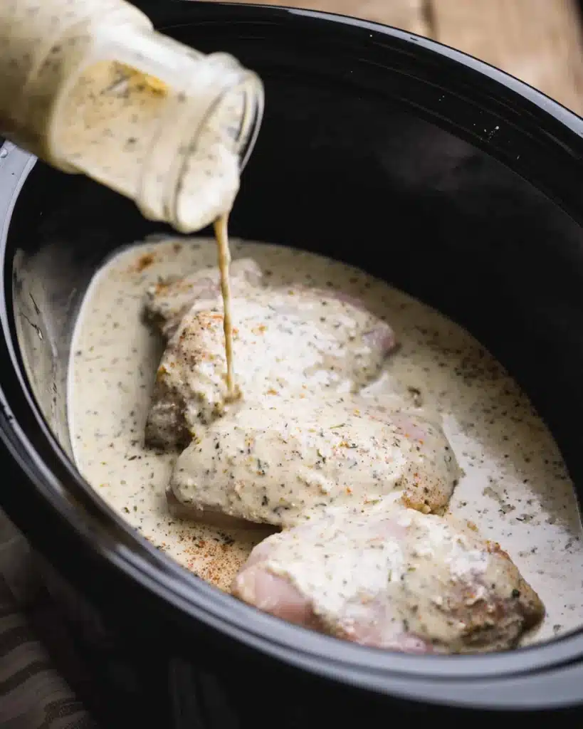 Crockpot Garlic Parmesan Chicken Pasta That's Creamy and Comforting 15 Pouring creamy parmesan garlic sauce over chicken breasts in a slow cooker.