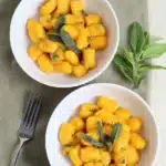 Golden pumpkin gnocchi with crispy sage in white bowls on a rustic table