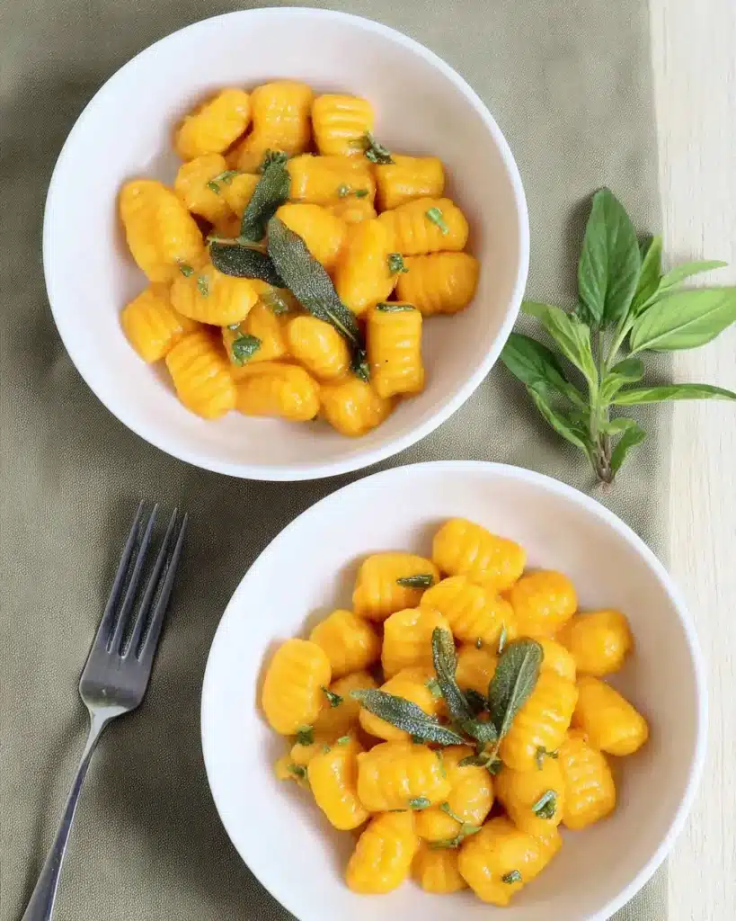 Golden pumpkin gnocchi with crispy sage in white bowls on a rustic table