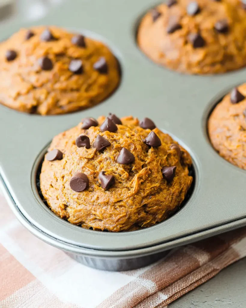 Pumpkin chocolate chip muffin in silver baking tin with melted chocolate chips on top

