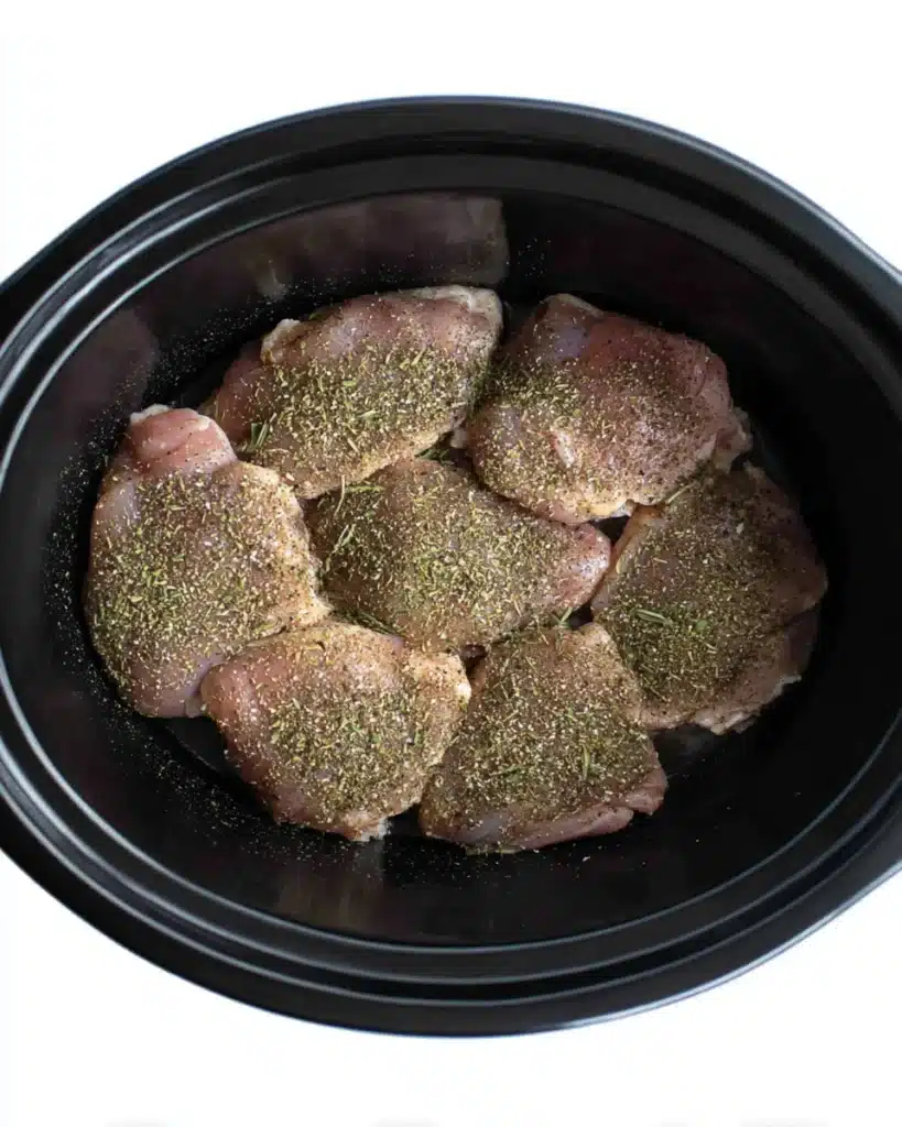 Raw seasoned chicken thighs arranged in a black slow cooker before cooking Tuscan chicken