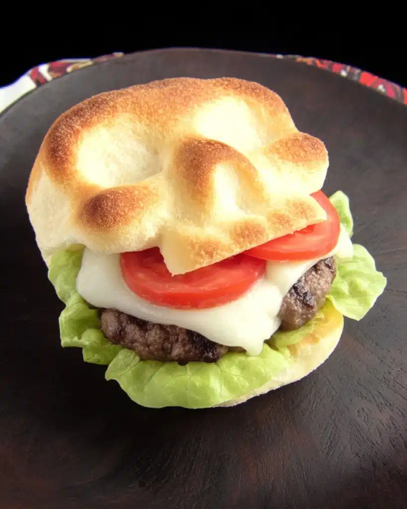 Skull-shaped cheeseburger with melted cheese, fresh tomatoes, and lettuce on a black plate