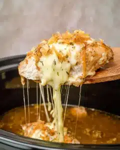 Melted provolone cheese stretching from Crock Pot French Onion Chicken with crispy onions on top